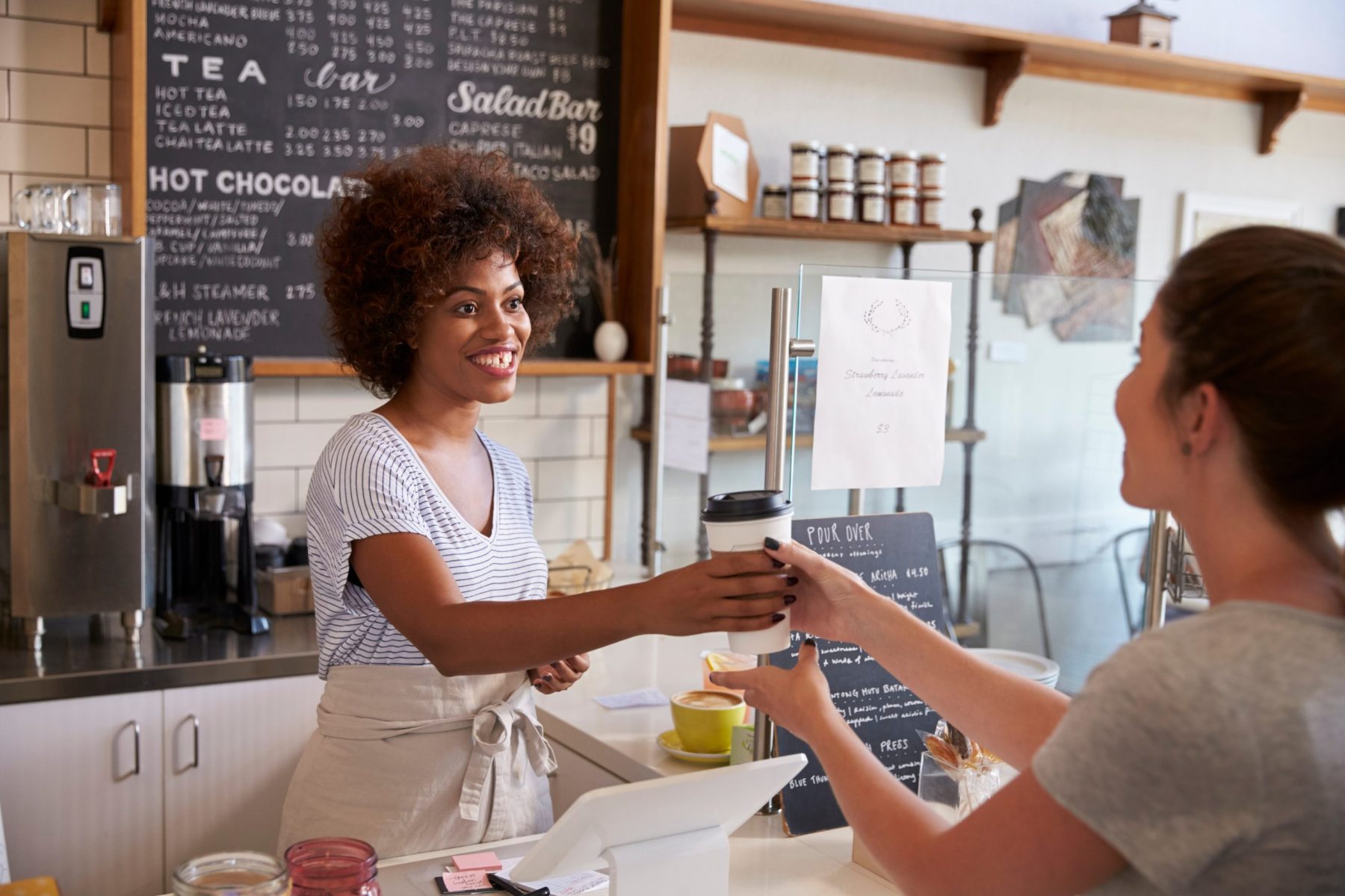 Waitress serving customer over the counter at a coffee shop in front of menu board restaurant sign
