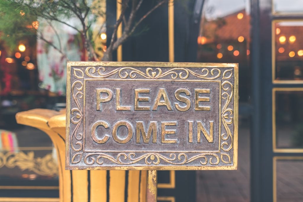 vintage copper sign on a store front saying "please come in"